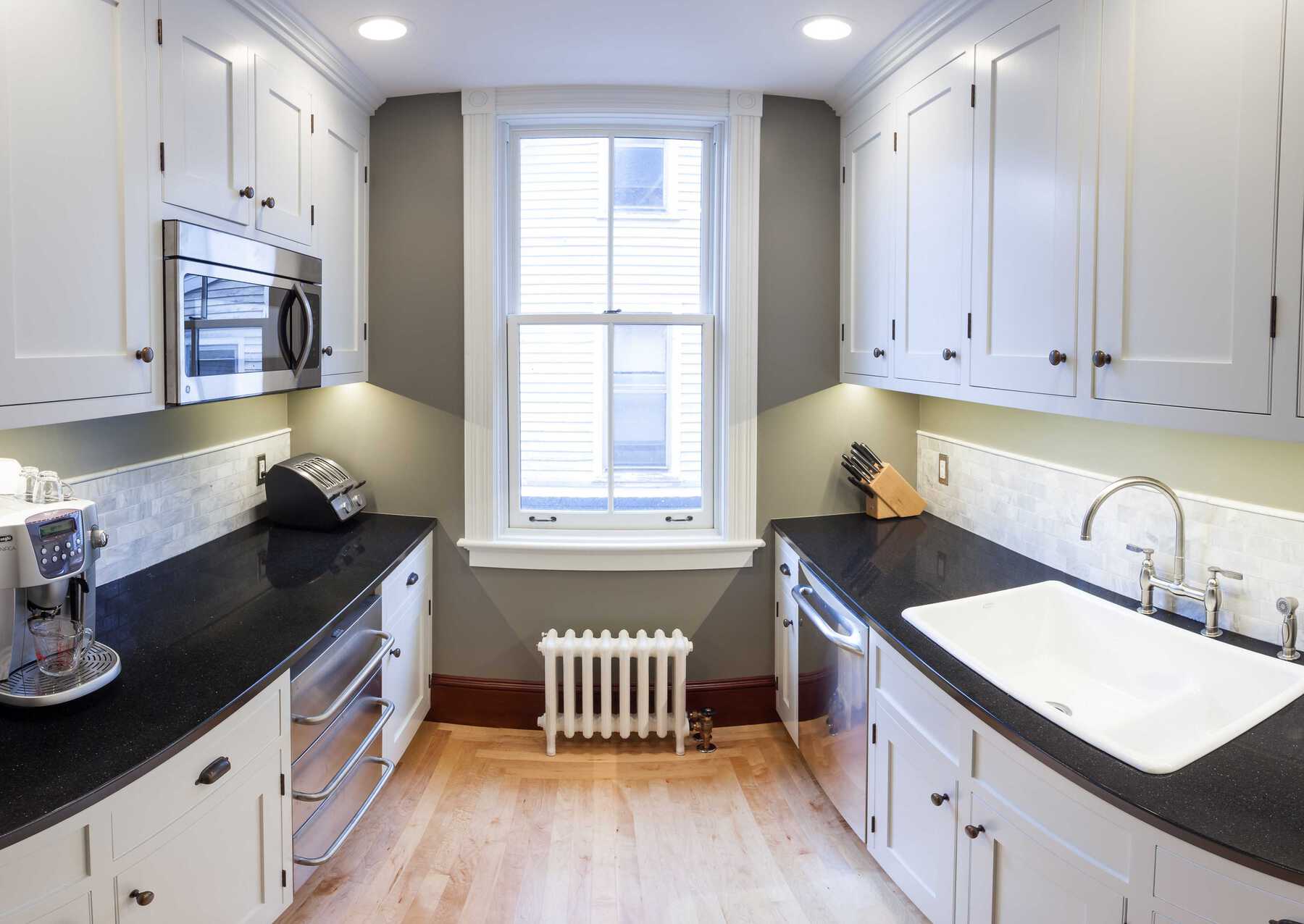 Small kitchen with wood floor, dark counter, and white cupboards