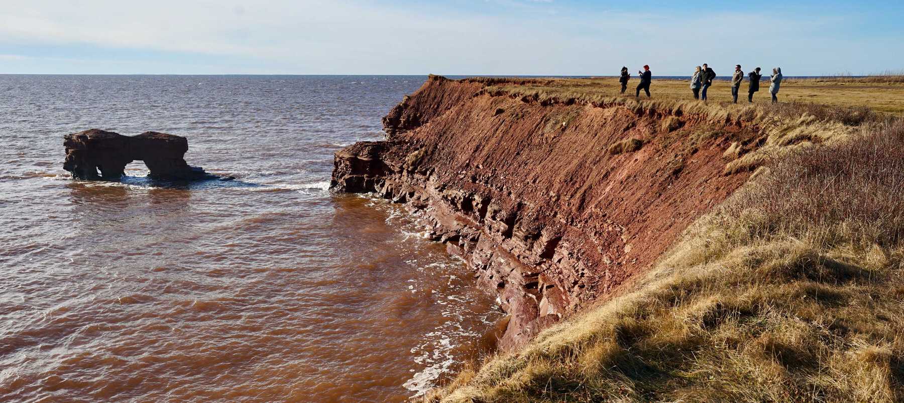 People standing near tall red clifs by ocean