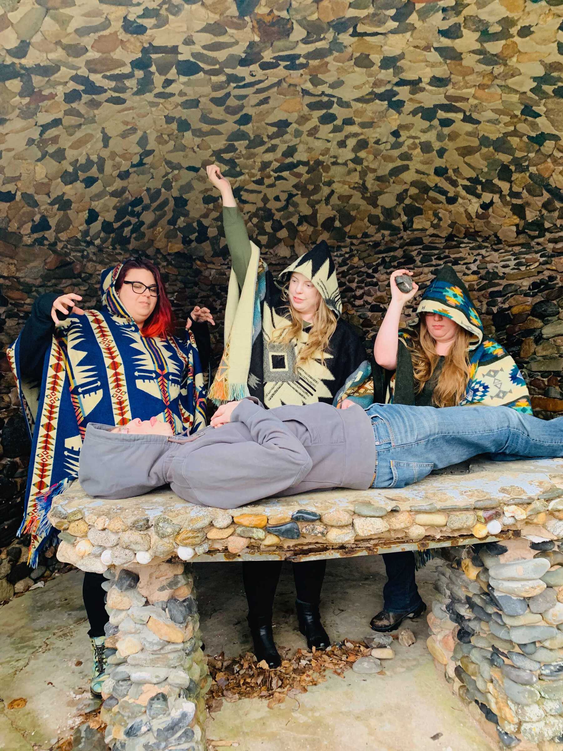 Three women in hoods pretending to sacrifice a man on an altar